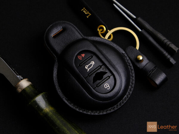 Handcrafted black Mini key fob cover with exposed button design, made of premium leather with gold hardware and precise stitching.