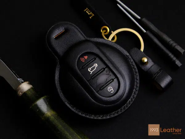 Handcrafted black Mini key fob cover with exposed button design, made of premium leather with gold hardware and precise stitching.