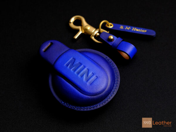 Blue leather Mini 5-Door key fob cover showcasing embossed MINI logo on the back, handcrafted with high-quality stitching.