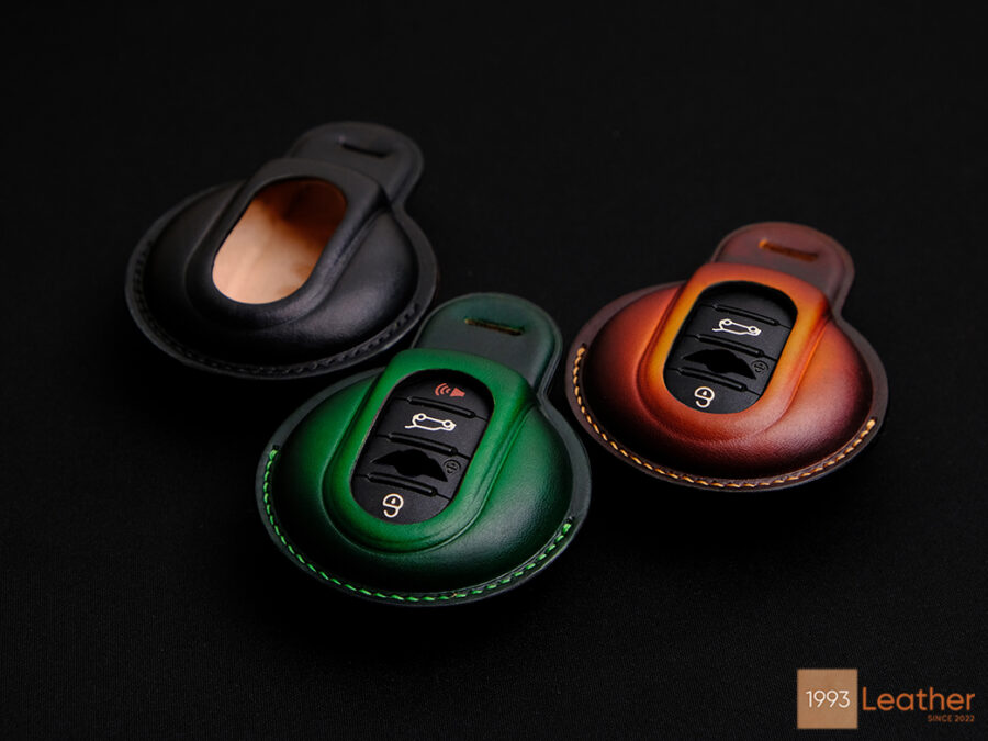 Mini JCW key fob covers with exposed button design in black, green, and patina brown leather, representing easy access and style.