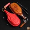 The premium leather key cover comes in various colors, featuring embossed button details and a personalized leather tag.