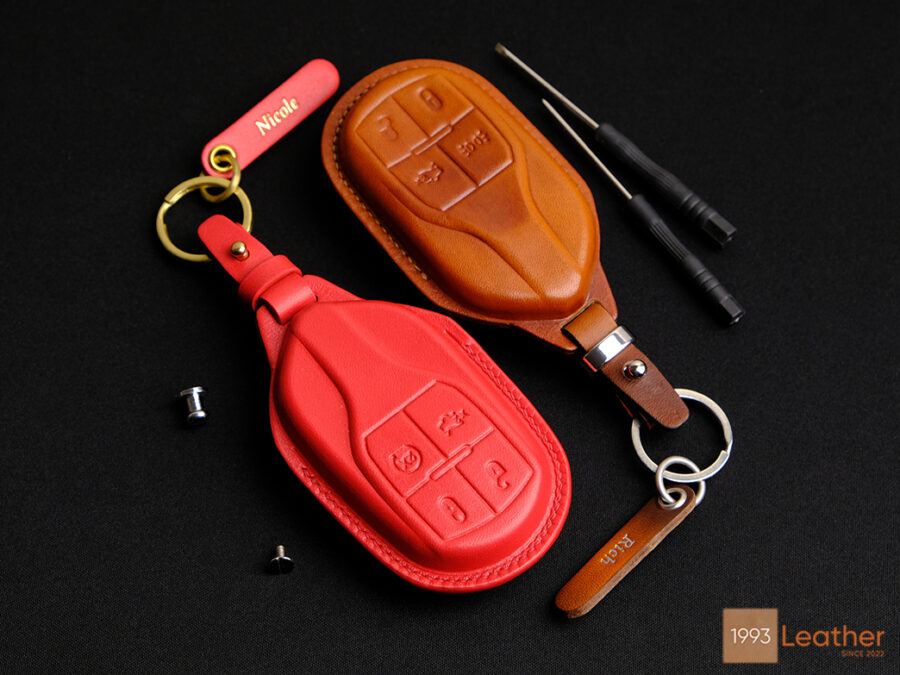 The premium leather key cover comes in various colors, featuring embossed button details and a personalized leather tag.