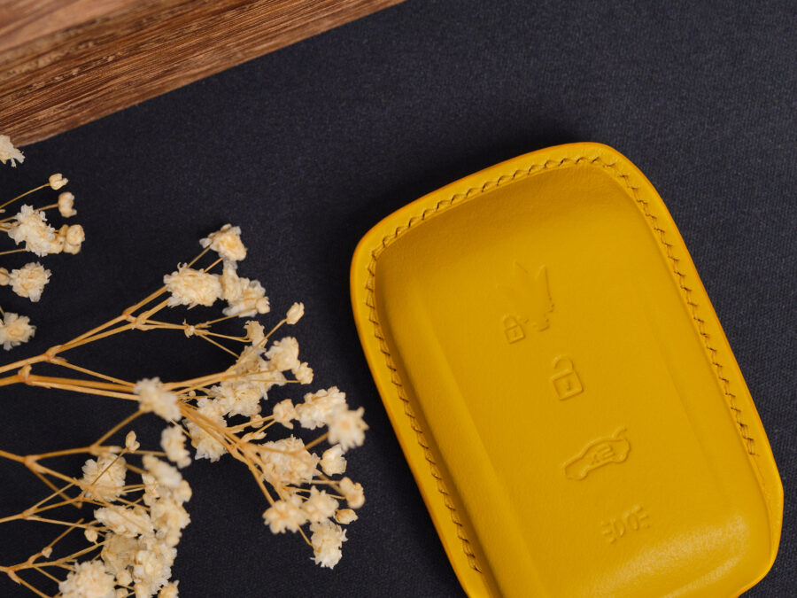Yellow leather Maserati Grecale key fob cover close-up showing button area and stitched edges