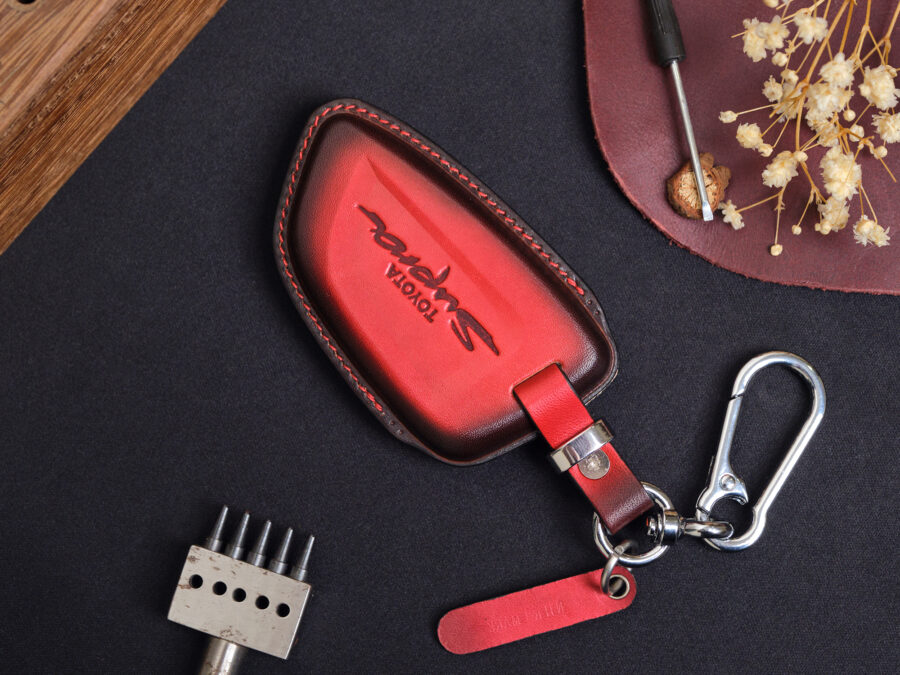 Red leather Toyota Supra key fob cover with embossed Supra logo, metal keyring, and matching leather tag