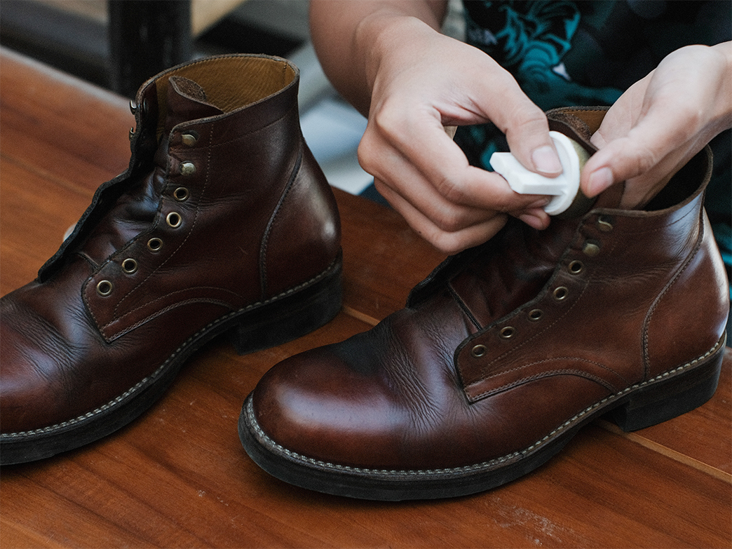 Polishing leather boots with mink oil in sponge wooden table